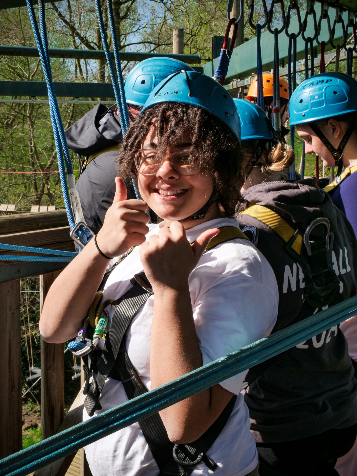 A girl with a helmet on smiling at the camera with her thumbs up