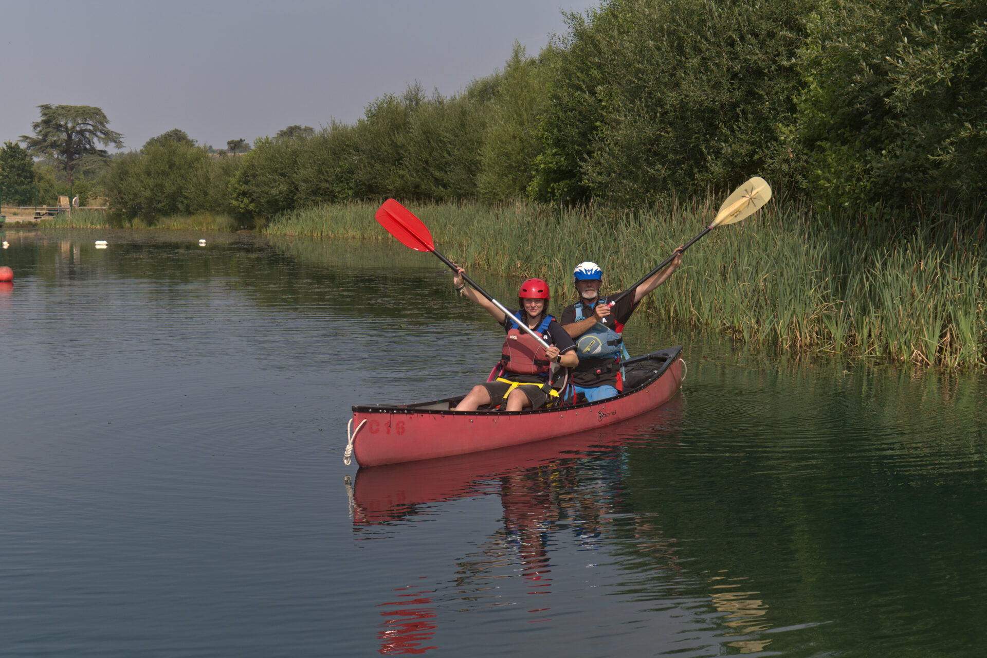 Young person and instructor raising paddles in celebration in a canoe on the lake