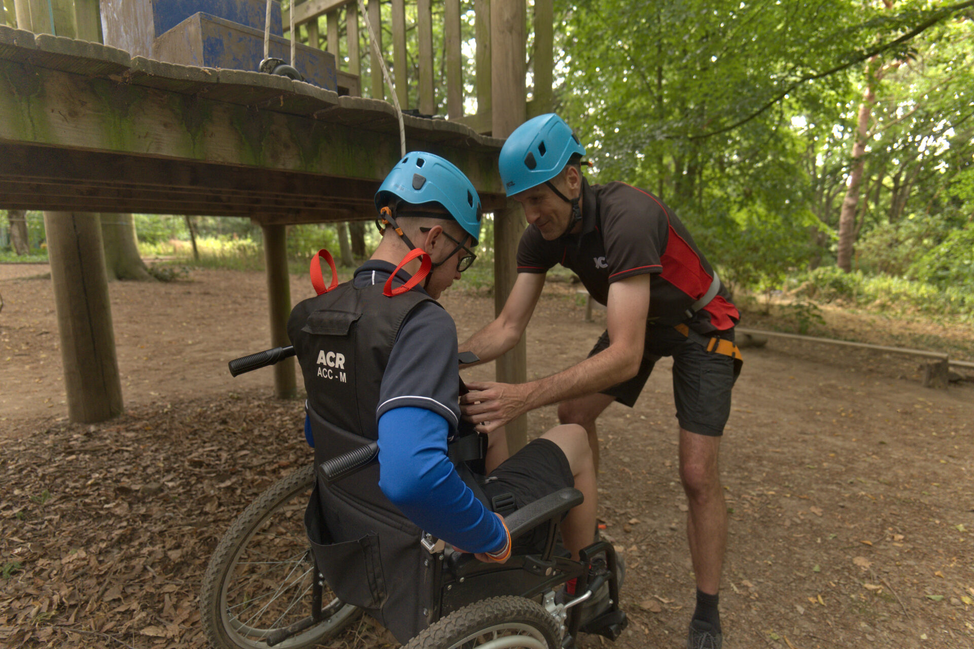 Wheelchair user being fitted with safety equipment before a high ropes activity