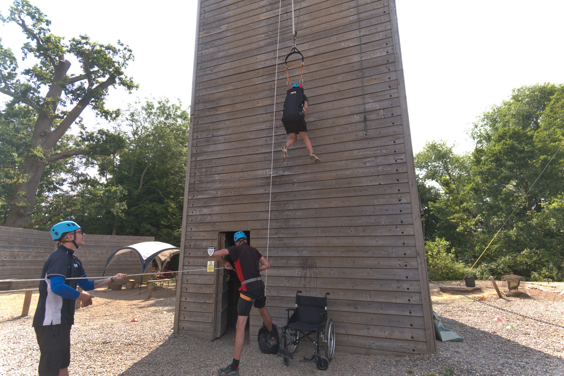 Team hauling a participant up the climbing tower in an adapted seat, with their wheelchair at the base