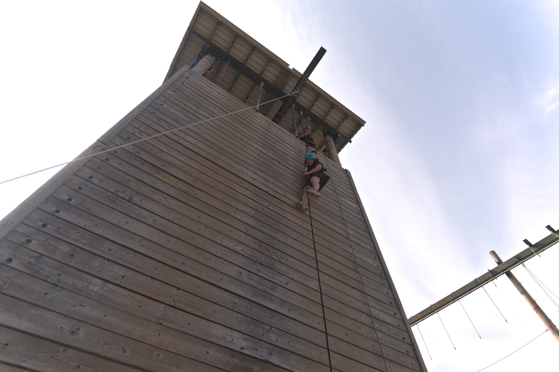 Participant abseiling down the tall wooden tower in an adapted harness