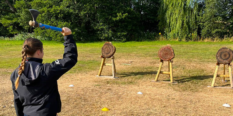 Girl in JCA gear throwing an axe at a wooden target Girl in JCA gear throwing an axe at a wooden target