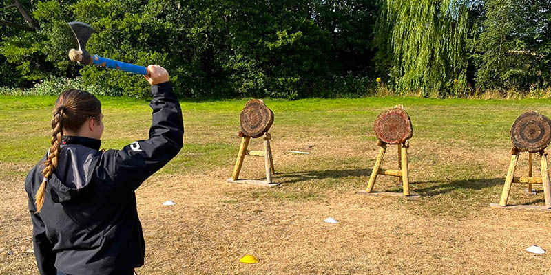 Girl in JCA gear throwing an axe at a wooden target