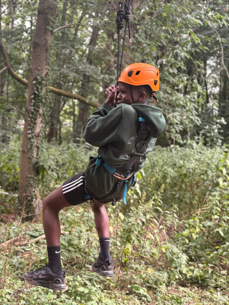 A young boy with an orange helmet on, mid-zipwire. He is not looking at the camera.