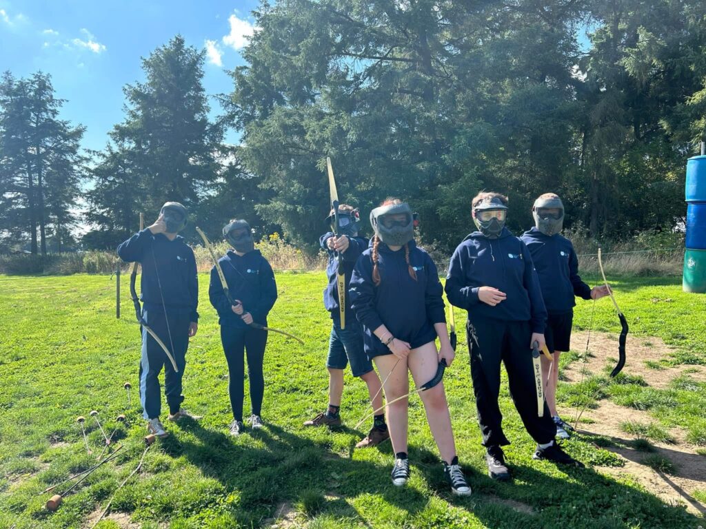 A group of 6 young people, with masks on and bows in hand, to start a game of archery.