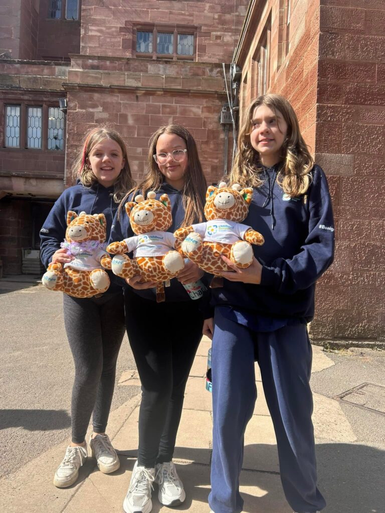 Three girls all in leggings and tracksuits, holding three giraffe toys.